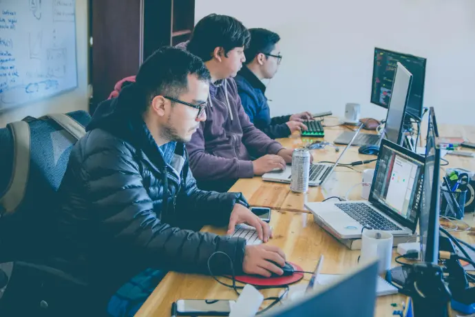 three men facing computer monitors